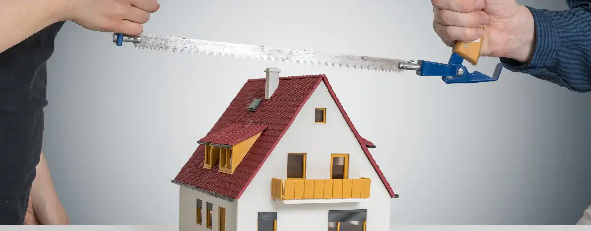 Who gets the house in a divorce? Two people sawing a toy house.